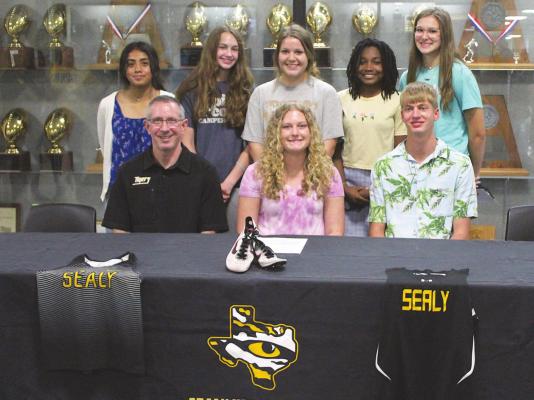 Sealy High School cross country runners (back row from left) Hailey Arteaga, Annabelle Williams, Trinity Anderson, Hollie Brown, Jenna Forrester and Cameron Eschenburg (right front), as well as head coach Anthony Branch (left front), celebrated Madison Manak’s (center front) signing to run for the Jacksonville Junior College Jaguars during a ceremony in the gym foyer last Wednesday, May 26. COLE McNANNA