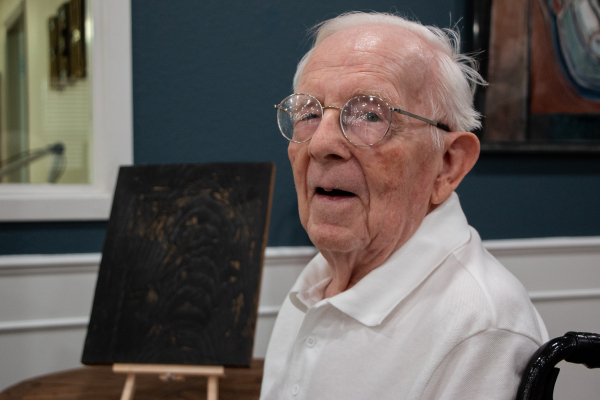 Surrealist artist Norman Baasch poses for a portrait in front of a linograph etching of a self portrait, Friday, June 27, 2025, at Avir at Sealy, in Sealy, Texas. Sealy News | Allison Drinnon