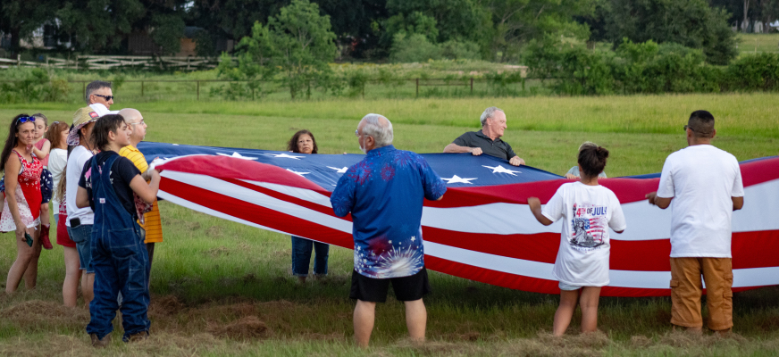 Sealy community members hoist up a large American flag for the national anthem at the Faith, Family and Fireworks event, Saturday, July 4, at Christian City Fellowship in Sealy.