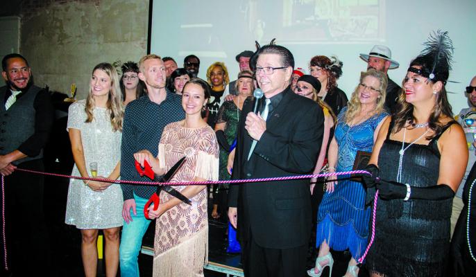 1910 owner Natalie DeJong prepares to cut a string to commemorate the event and building with dressed up community members in the back Brandt. PHOTO BY ABENEZER YONAS