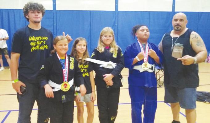 Sealy BJJ coaches Conner Bilyeu, left, and Kenneth Amador, right, led three athletes through the Grappling Summer Slam tournament at the Zone Sportsplex in Houston last weekend. Zoe Clark, second from left, and Ysrael Trevino, second from right, won their brackets while Lydia Clark finished fifth in her second tournament appearance for Sealy BJJ. COURTESY PHOTO