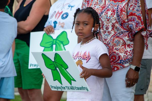 Kaisley Brown holds up a sign with a green ribbon while waiting with her mother and grandmother for the funeral procession of Camp Mystic camper Virgina Hollis, Wednesday, July 16, at Faith Academy in Bellville. A green ribbon has become a sign of support for those affected by the flooding in the Texas Hill Country. 