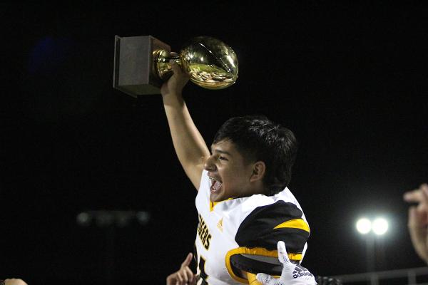 Sealy senior Oswaldo Rodriquez is hoisted upon his teammates' shoulders holding the trophy following the Tigers' 21-19 win over Silsbee Friday night in the first round of the playoffs. COLE McNANNA