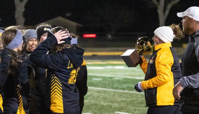 Lady Tiger Head Soccer Coach Sydney Jones brings the regular-season district championship trophy into a huddle of Sealy players after the season-ending win over Royal at T.J. Mills Stadium March 11. Jones was named the District 24-4A coach of the year. PHOTOS BY COLE McNANNA