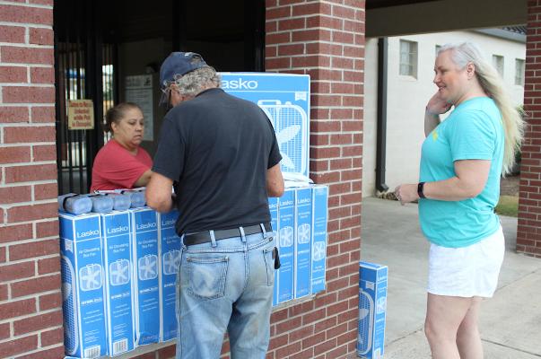 Combined Community Action Executive Secretary Dalila Mansiya, left, and Communication Director Karen Walpole, right, assist an Austin County resident with the pickup of heat-preventative items outside LeBlanc Pool in Sealy Monday morning. COLE McNANNA