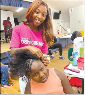 Hairstylist Brushed by Oshi the Chemist braids the hair of Sealy ISD first grade Ariana Wolfe.