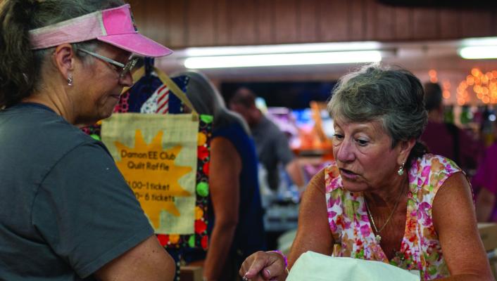 Cherrie Ziese explains how she makes her canvas tote bags to Tracey Zientek at the Wallis American Legion Post 200's 22nd Annual Arts and Crafts Show, Saturday, July 12, at the Wallis American Legion Hall. Ziese embroidered the bags with simple illustrations and quotes.