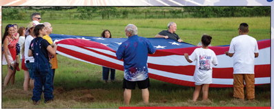 Sealy community members hoist up a large American flag for the national anthem at the Faith, Family and Fireworks event, Saturday,
