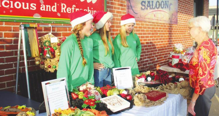 Jacie Kainer, Avery Grigar, and Jade Barton explained their decorative wreath business, RoseMaLeigh, to guests outside of Saddleback Saloon Bar and Grill during Vendor Blender last Thursday. HANS LAMMEMAN