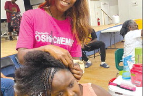 Hairstylist Brushed by Oshi the Chemist braids the hair of Sealy ISD first grade Ariana Wolfe.