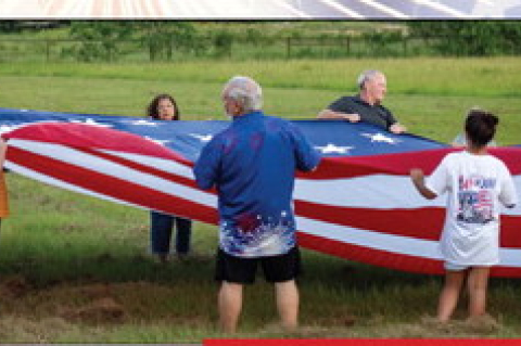 Sealy community members hoist up a large American flag for the national anthem at the Faith, Family and Fireworks event, Saturday,